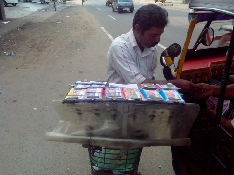A Kerala street vendor selling printed lottery tickets from a bicycle display.
